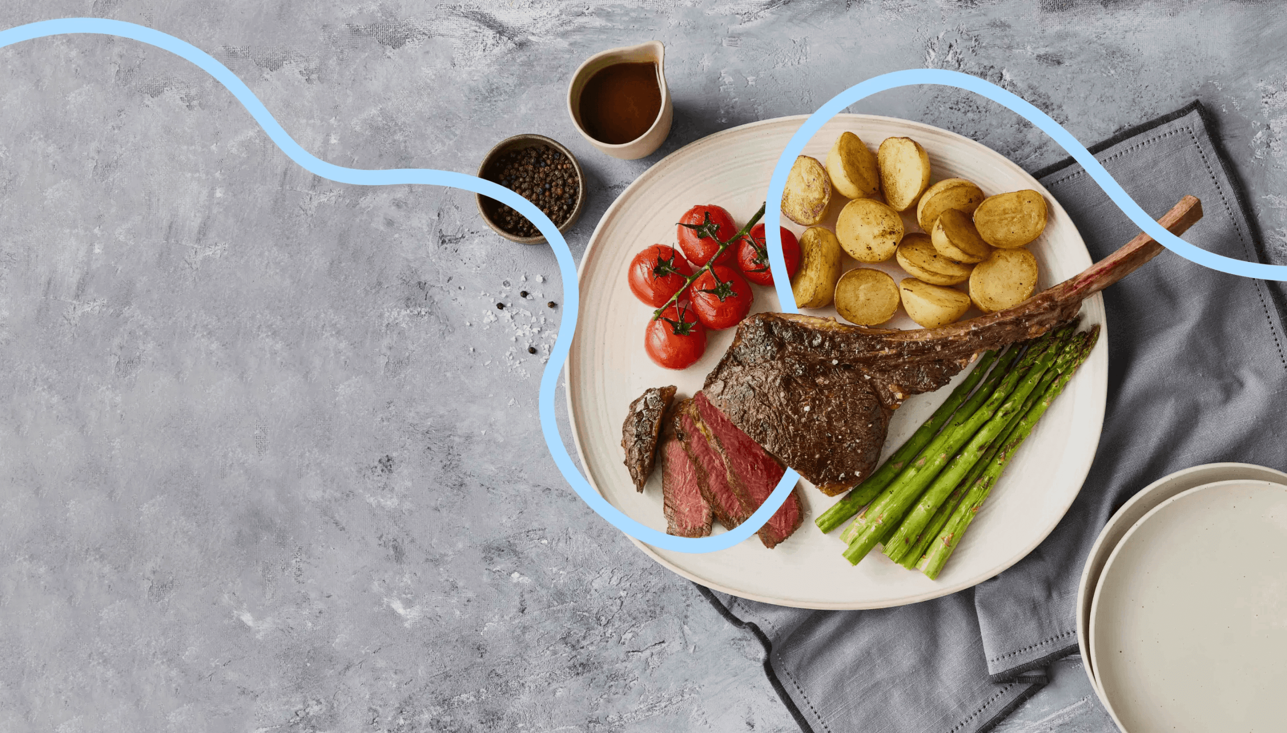 A plate with grilled steak, asparagus, roasted potatoes, and tomatoes sits on a gray surface with a napkin, sauce, and pepper nearby. A blue wavy line overlays the image.