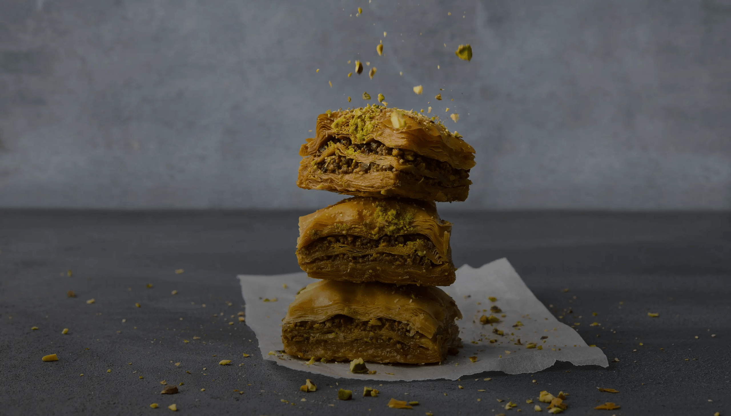 Stack of baklava topped with pistachios on parchment paper.