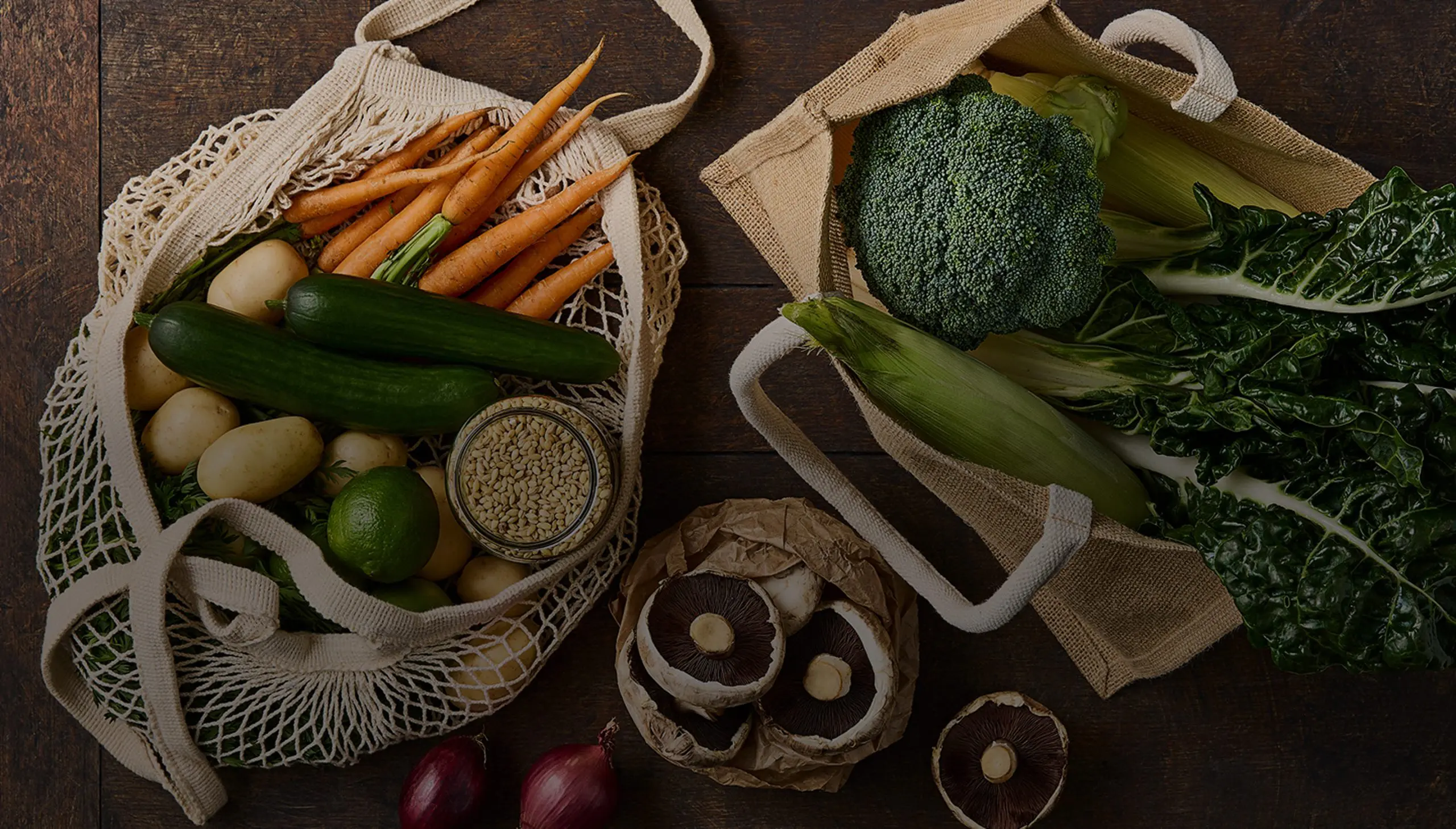 Fresh vegetables in reusable bags: carrots, potatoes, broccoli, mushrooms. Promotes sustainability.
