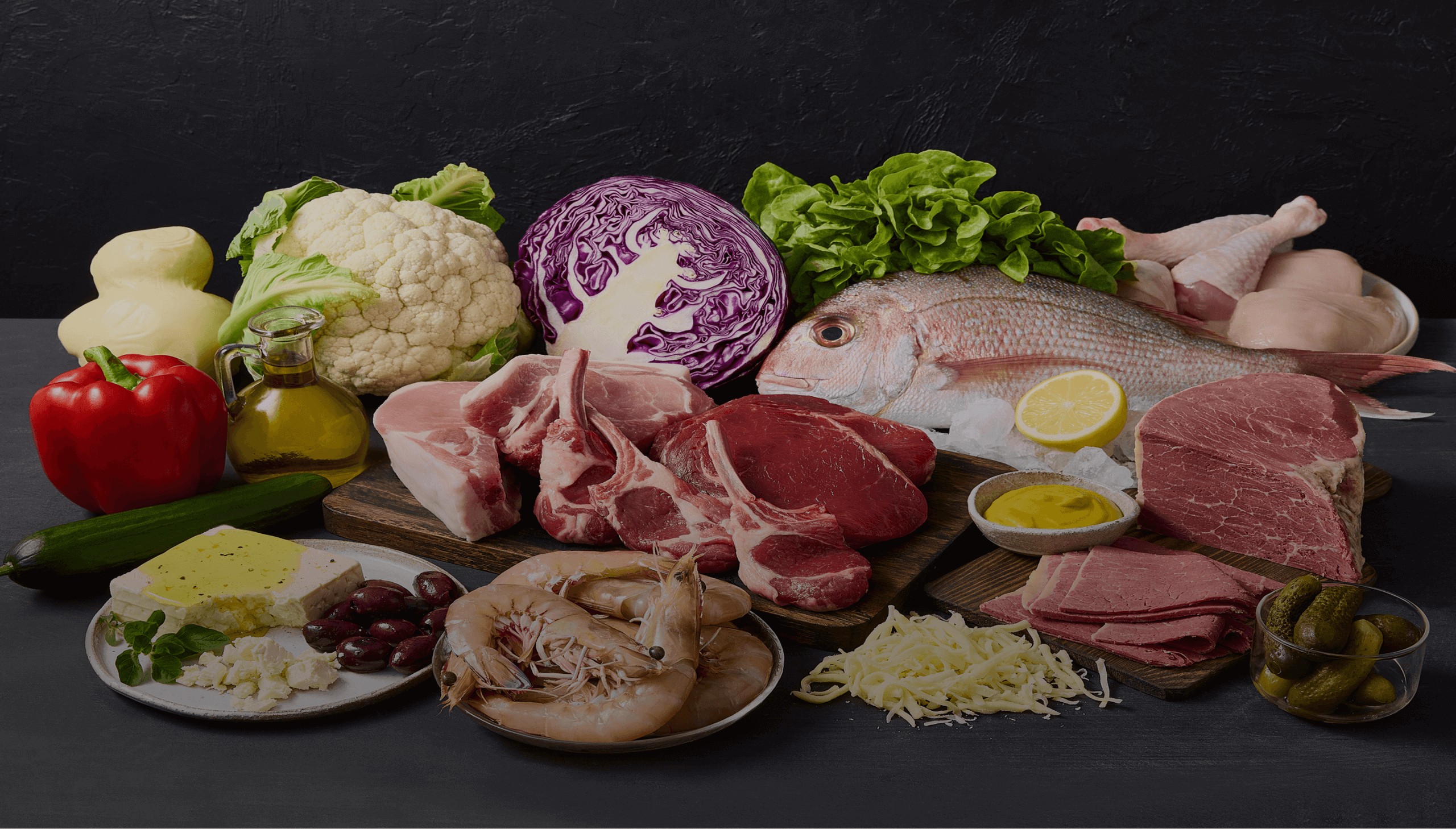 Variety of whole foods: meat, fish, seafood, cheese, and fresh vegetables on a dark background.