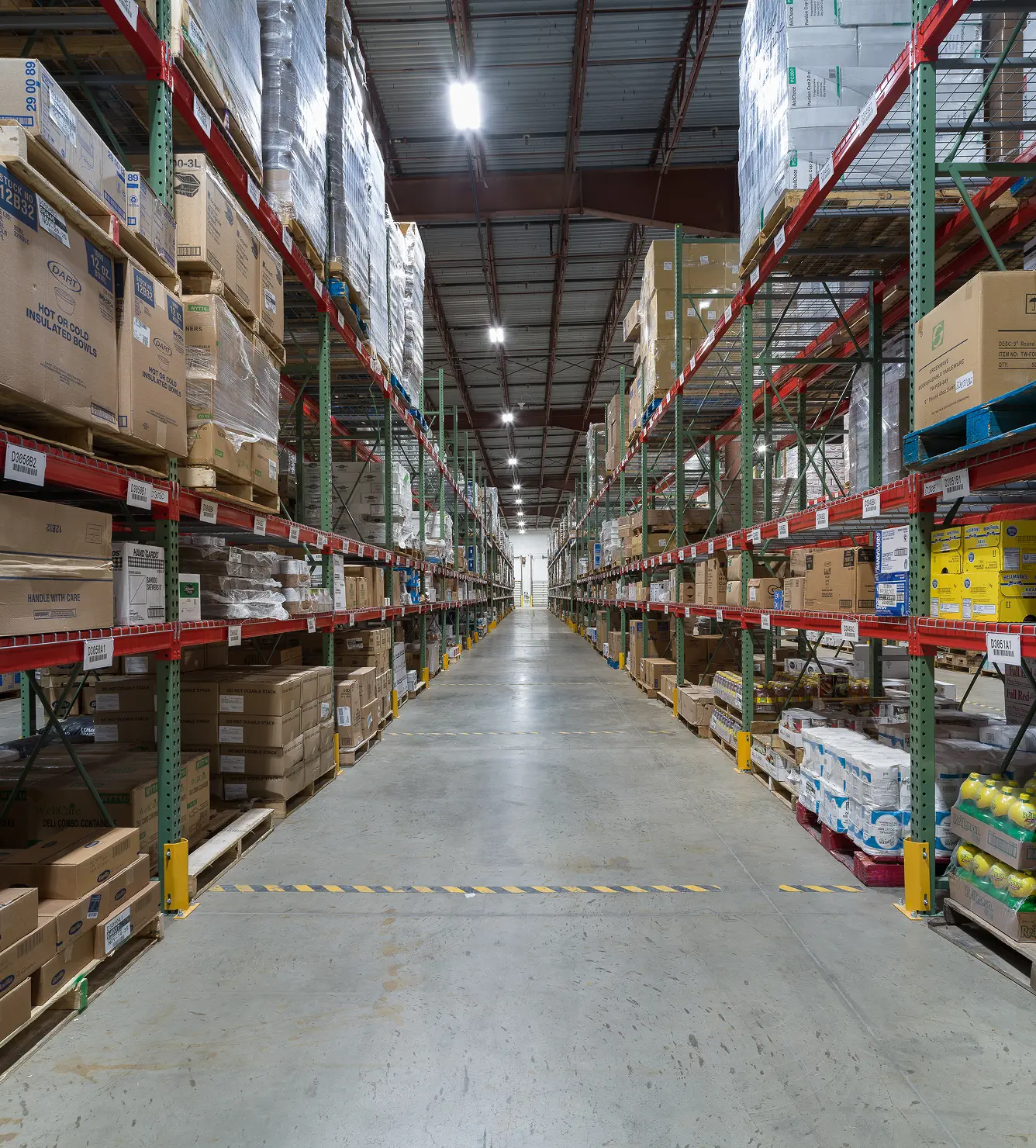 Warehouse aisle with shelves stocked with food and supplies, including Dart insulated bowls and tableware.