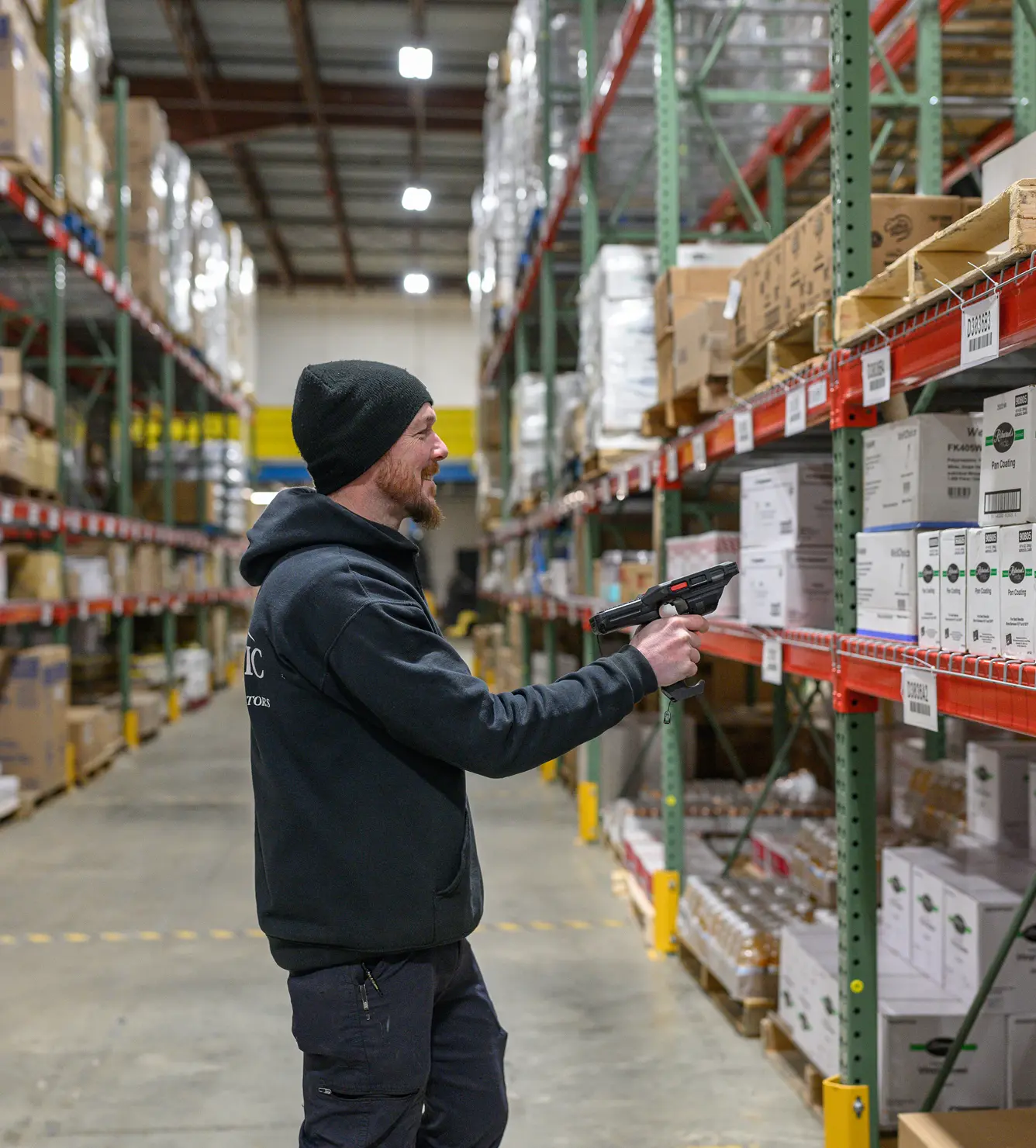 Man scanning boxes in a large warehouse with stocked shelves. Inventory management.
