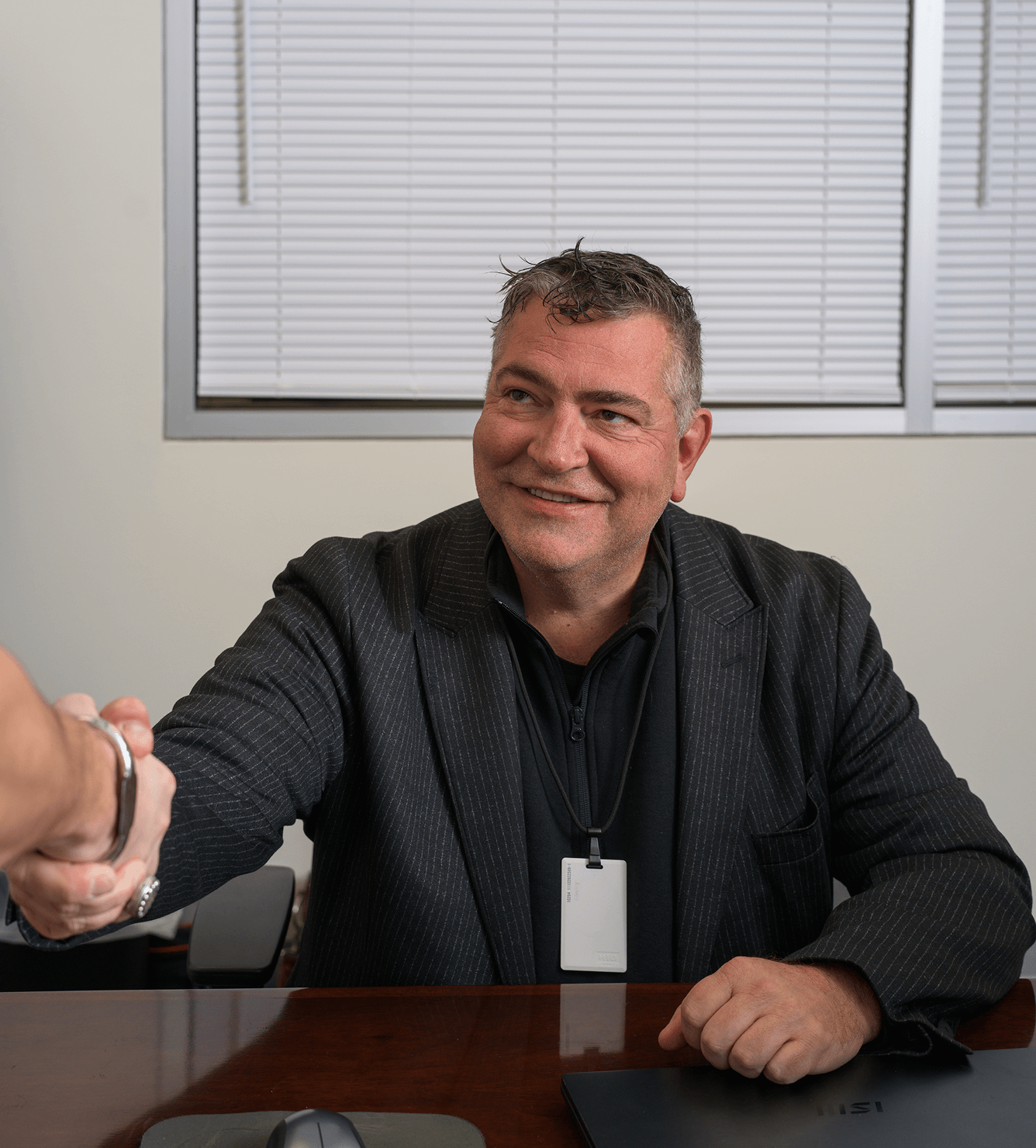 Man in suit shaking hands at desk with ID badge