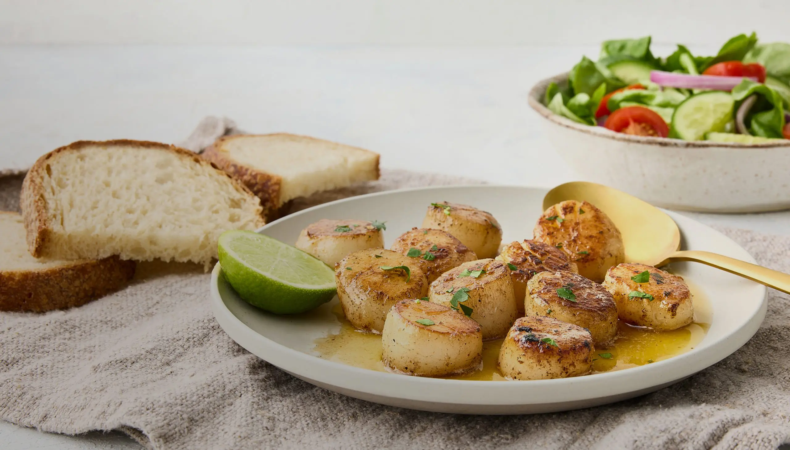 Seared scallops with lime, bread, and salad. Delicious seafood dinner.
