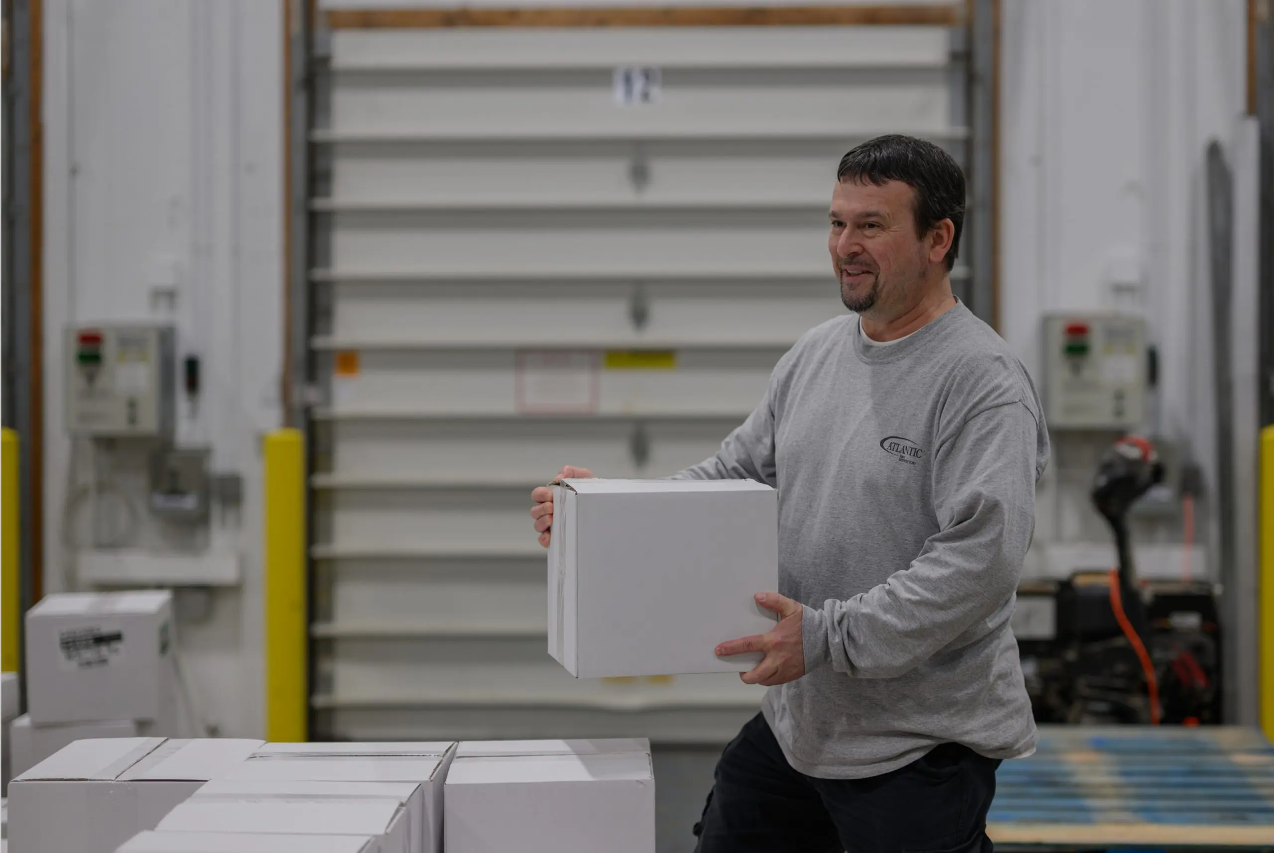 Warehouse worker lifting a white box in a distribution center, showcasing efficient logistics and inventory management in a commercial environment.