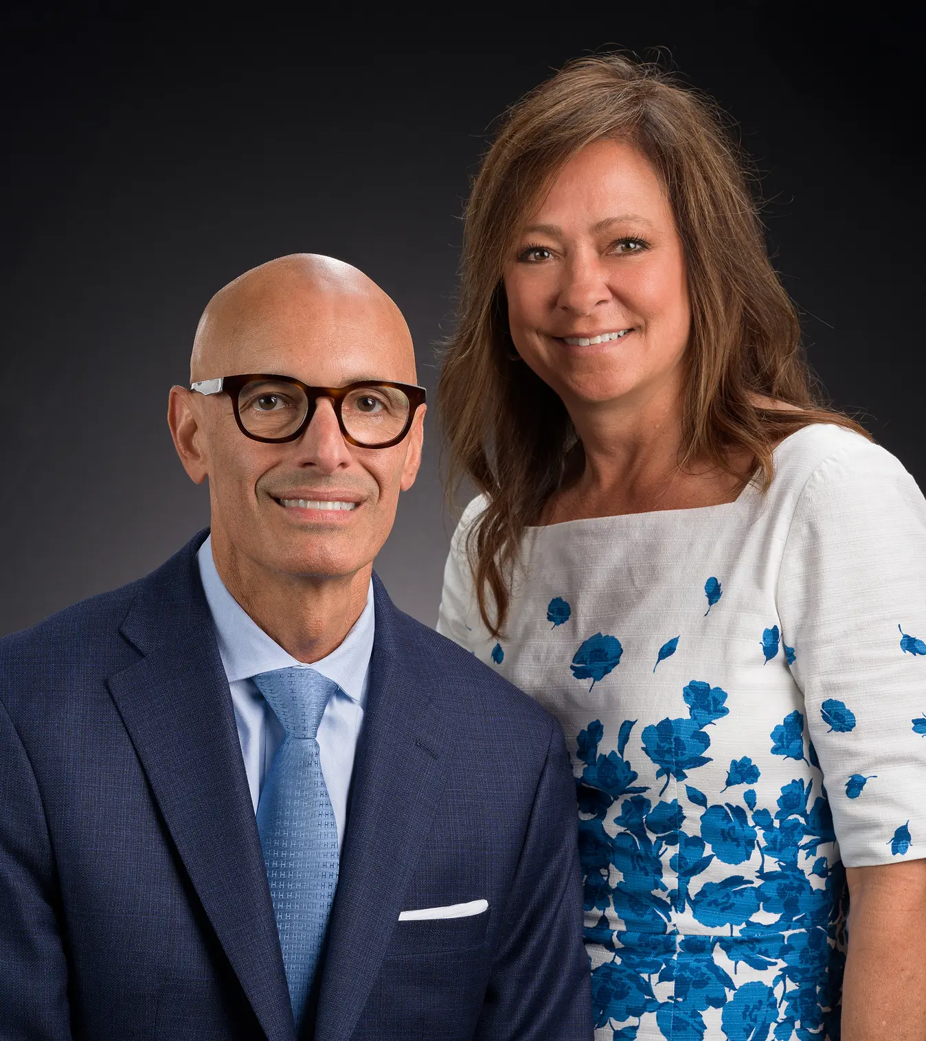 Professional headshot of a man in a suit and a woman in a floral dress.