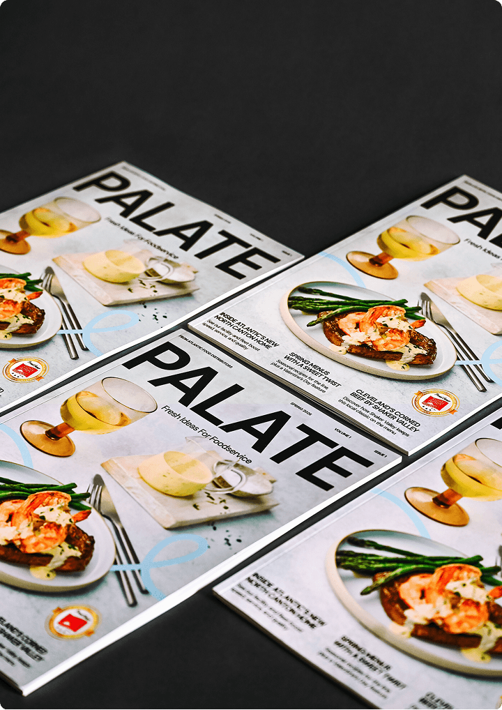 Stack of "PALATE" food magazine issues featuring vibrant dishes, including shrimp and asparagus, with drinks, showcasing fresh ideas for foodservice.
